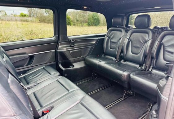 Interior of a spacious vehicle with black leather seats arranged in rows.